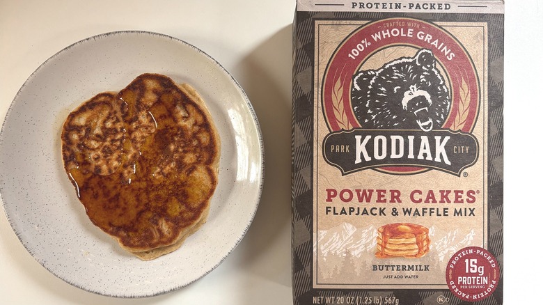 Kodiak Power Cakes Flapjack mix next to plate with cooked pancake on white table