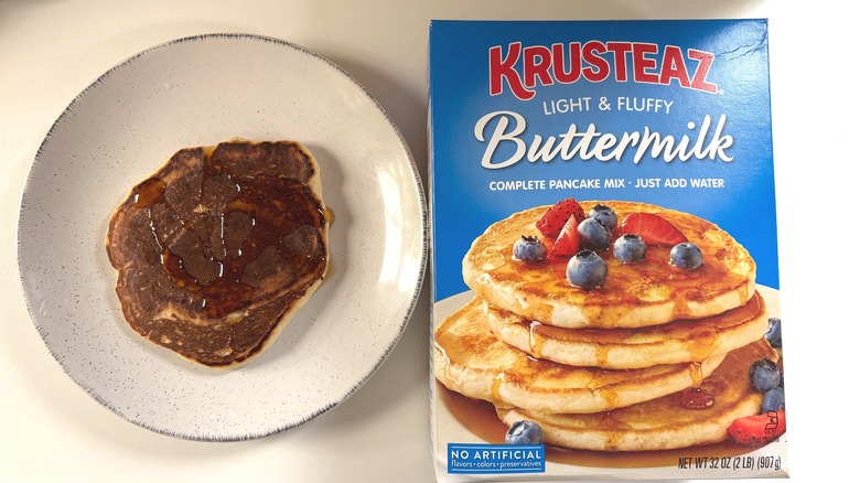 Krusteaz Light & Fluffy buttermilk pancake mix next to plate with cooked pancake on white table