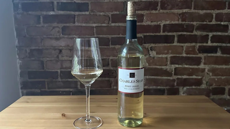Charles Shaw Pinot Grigio in a bottle and glass on a wooden table