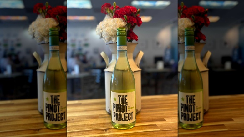 The Pinot Project Pinot Grigio bottle on a wooden table with flowers