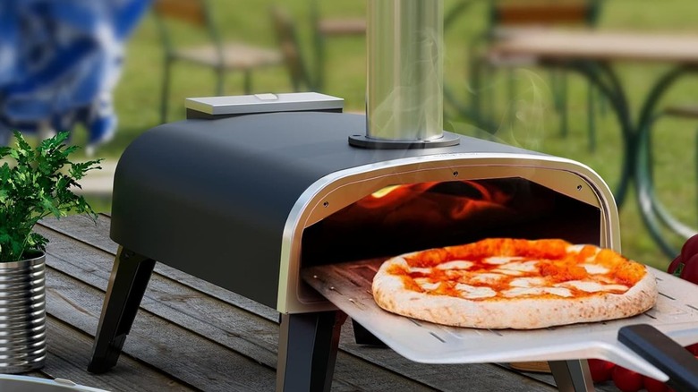 A pizza being pulled out of an Aidpiza pizza oven