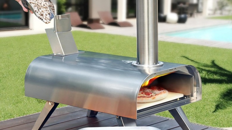 A person pouring wood pellets into a Big Horn Outdoors pizza oven