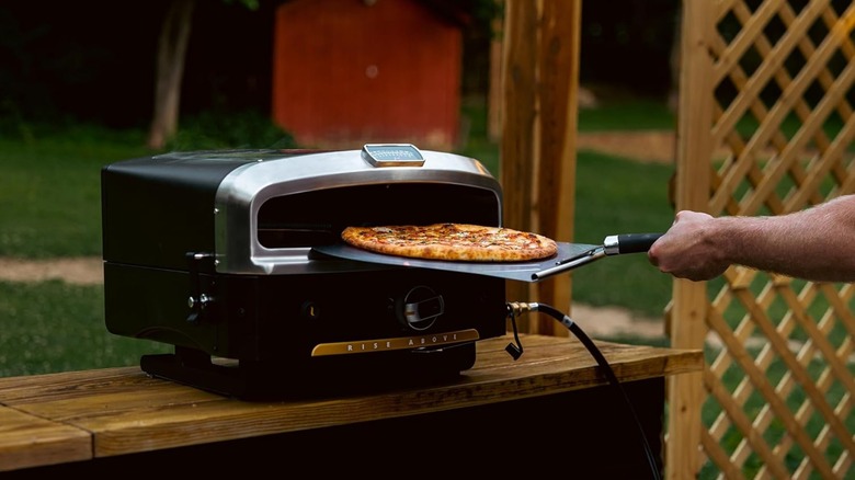A pizza being pulled out of a Halo Versa pizza oven