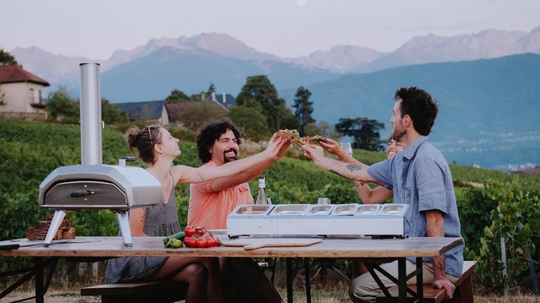 Friends eating pizza outside by an Ooni Karu pizza oven