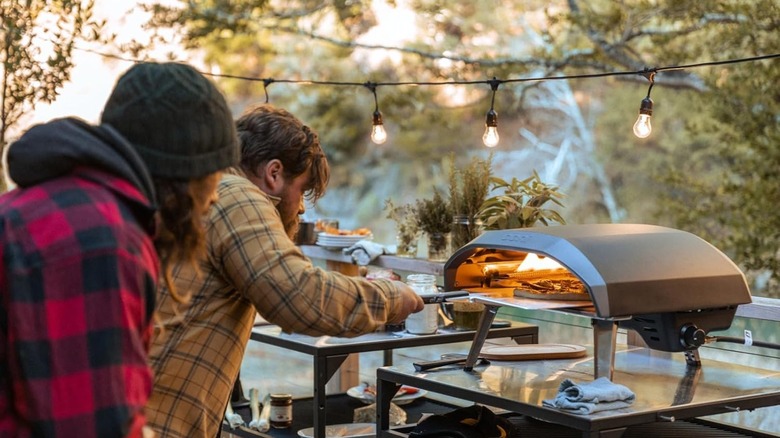 A person pulling a pizza out of an Ooni Koda pizza oven