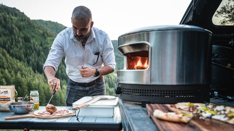 A man making a pizza by a Solo Stove pizza oven