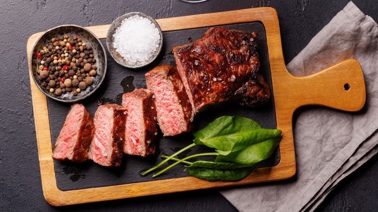 Overview of sliced steak on a cutting board with spices and greens