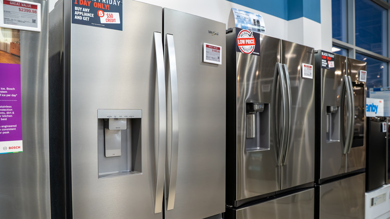 Three stainless steel refrigerators displayed in a row inside store with price stickers on the front