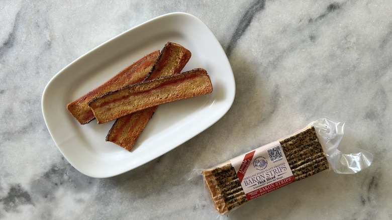 Thrilling Foods Bacon Strips, cooked on a white plate alongside the package