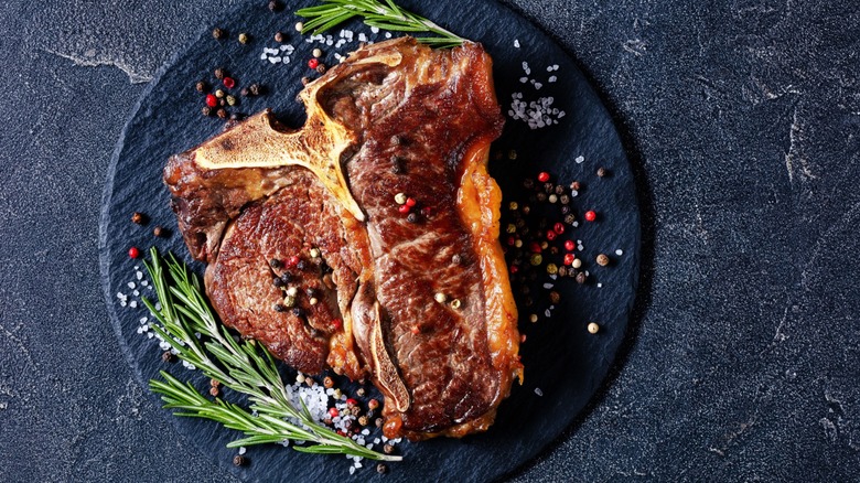 A cooked porterhouse steak on a plate with springs of herbs beside it