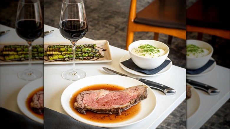 Prime rib with seprate plates and bowl with asparagus, mashed potato, and glass of wine