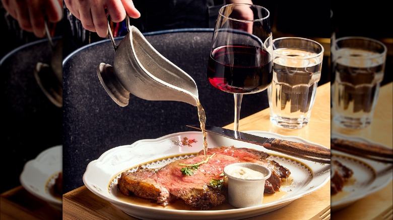 Pouring aus jus over prime rib beside wine and water glass