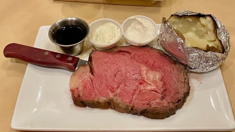 Prime rib on plate with baked potato, butter, horseradish, and aus jus