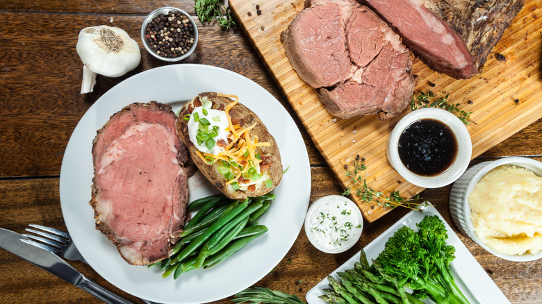 Whole prime rib being carved and plated with loaded baked potato and green beans