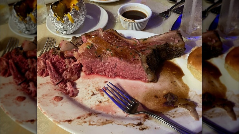 Partially-eaten prime rib with side plate of baked potato and au jus cup