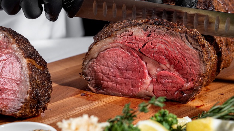 Prime rib being sliced on wooden board