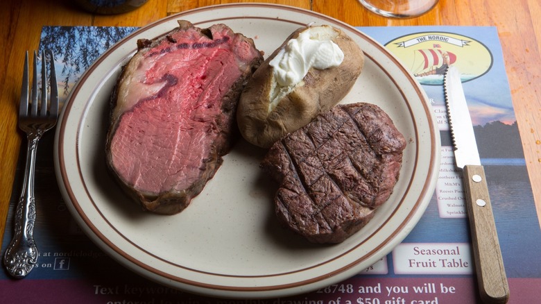 Prime rib, steak, and baked potato on plate with utensils