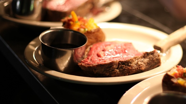 Plates of prime rib waiting at the pass with baked potatoes and au jus