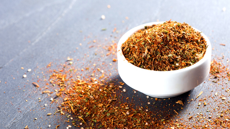 Bowl of chimichurri spice rub in a white bowl with some spice blend on a dark table