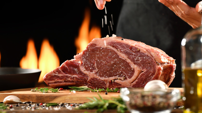 Chef sprinkling salt over raw prime rib displayed on a wooden cutting board