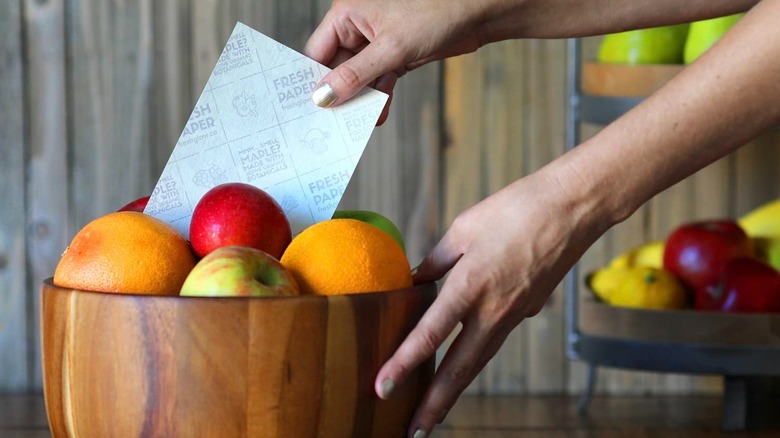 A person putting a Freshglow Freshpaper in a fruit basket