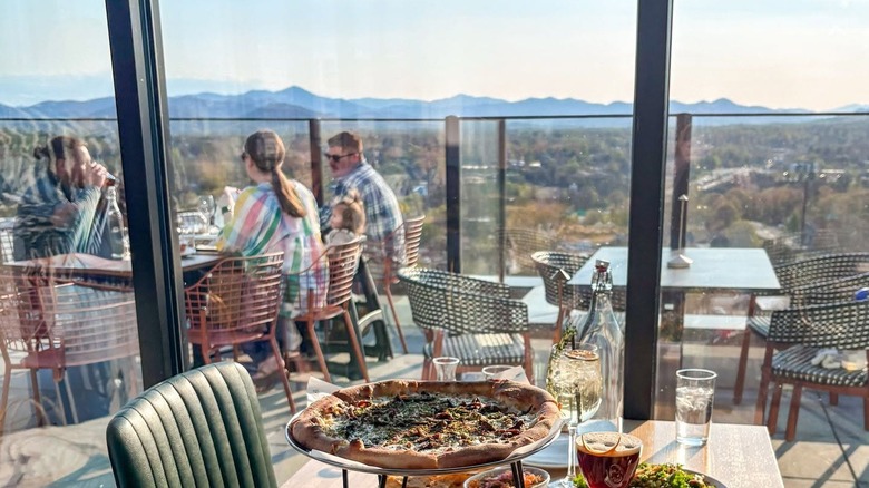 People dining on a restaurant terrace with distant mountain views in the background