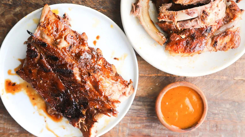 Baked and Grilled Baby Back Pork Ribs on white plates with bowl of sauce