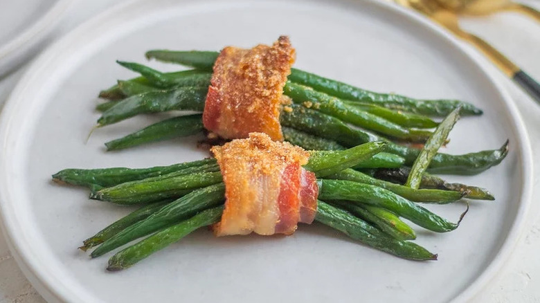 Two bacon-wrapped bundles of green beans served on a white plate
