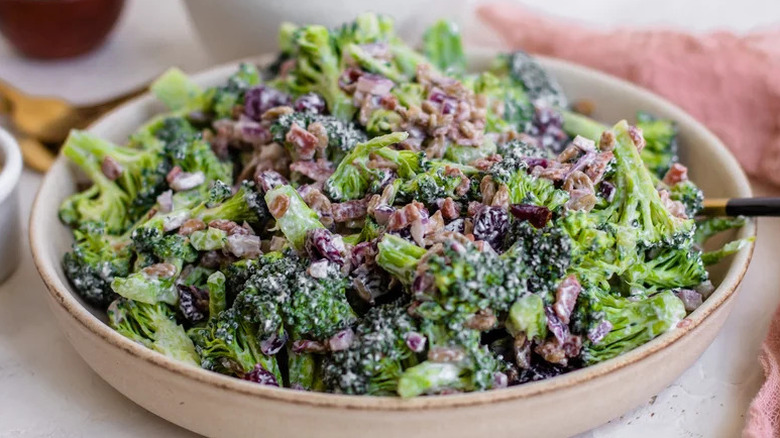 Bowl of creamy broccoli salad with bacon bits served in a beige bowl