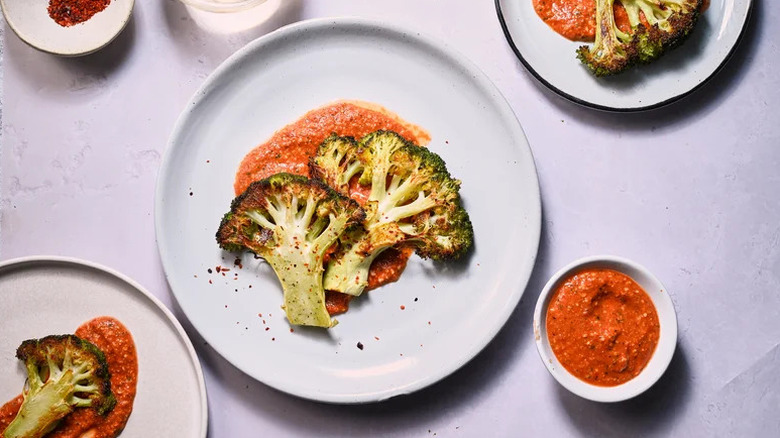 Broccoli steaks on plates with romesco sauce with more sauce in a separate bowl