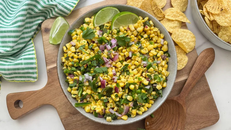 Bowl of corn salsa with red onion, cilantro, and lime wedges