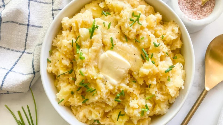 Bowl of creamy mashed potatoes topped with pat of butter and chopped chives
