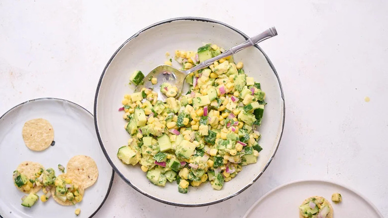 Cucumber, corn, and avocado salsa in bowl with spoon with chips on the side