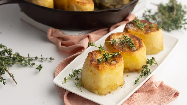 Fondant potatoes on white rectangular plate, topped with thyme sprigs