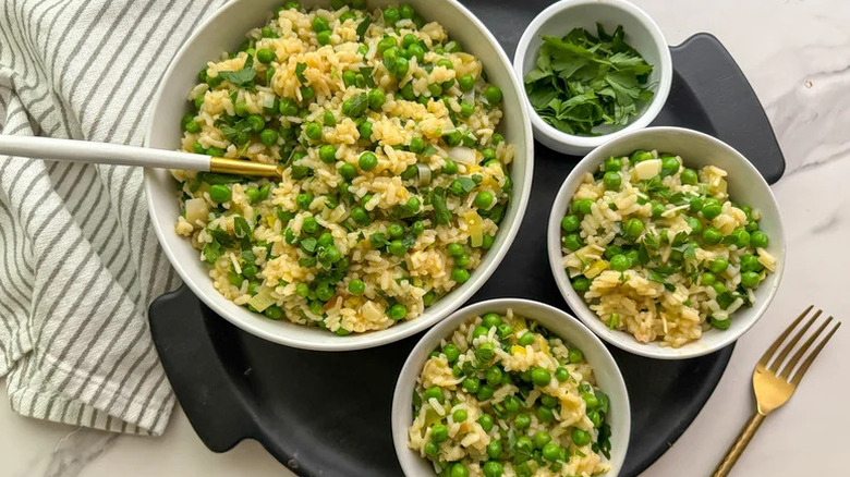 Rice dish with peas and parsley served into bowls garnished with fresh parsley with more parsley in a bowl