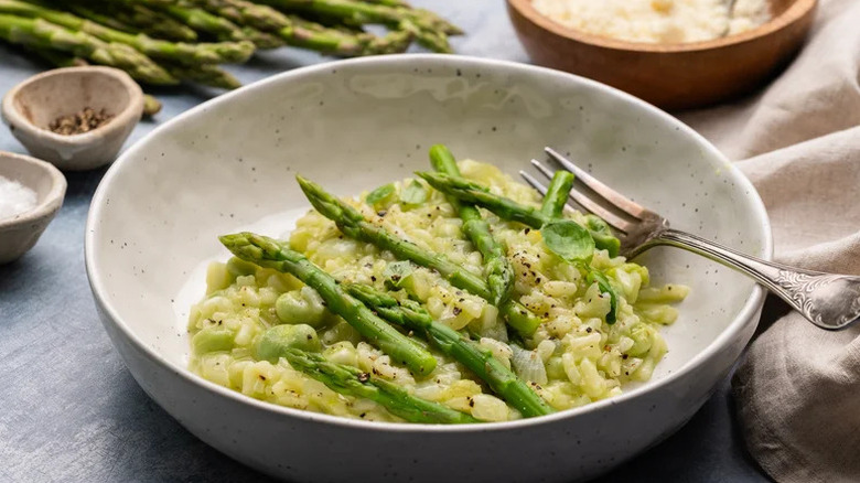 Asparagus and broad bean risotto in bowl with fork topped with cracked black pepper