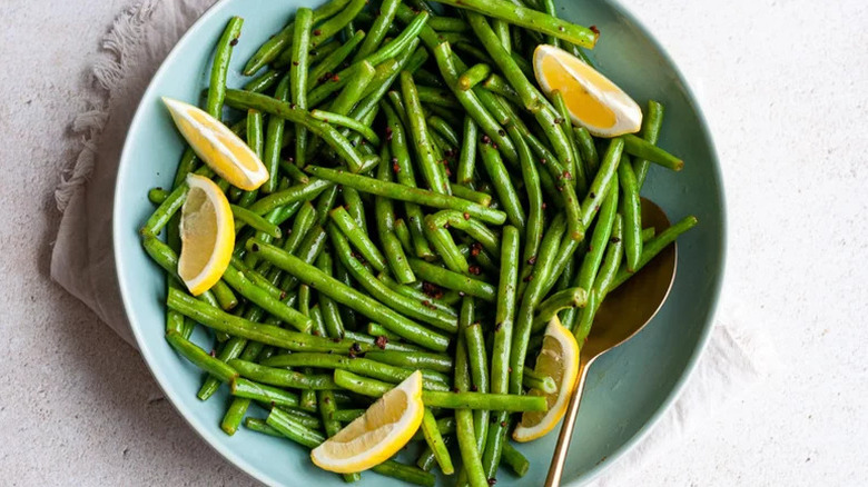 Sauteed green beans in blue bowl with lemon wedges and seasonings