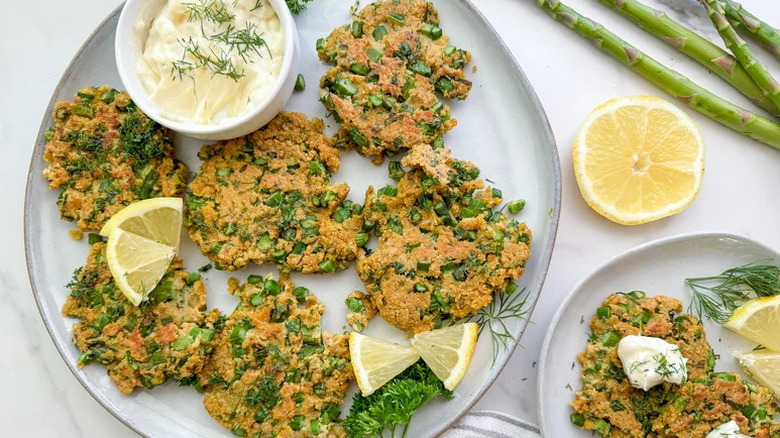 Lemon and asparagus fritters on plate with lemon slices and pot of creamy dip surrounded by lemons and asparagus