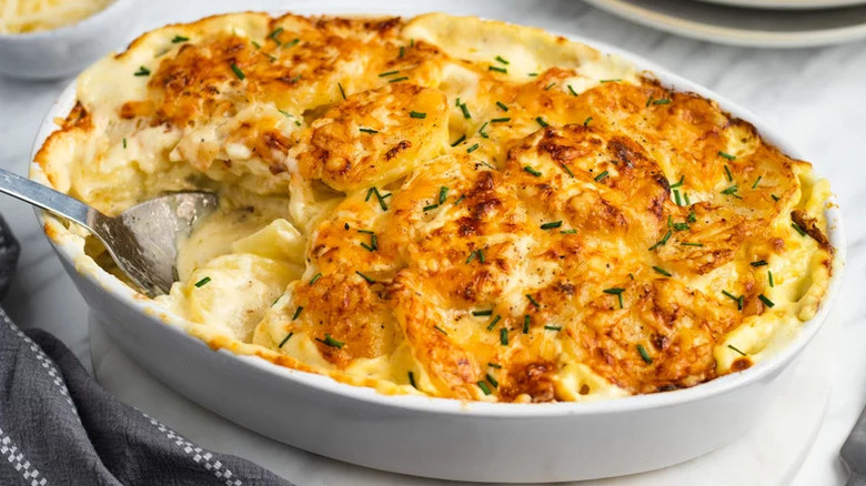 Potatoes au gratin in white baking dish with spoon garnished with greens