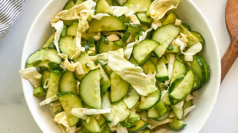 Top view of cucumber and kimchi salad in white bowl with wooden utensil on the side