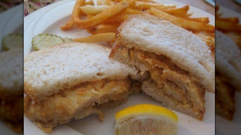 Fried fish sandwich on white sourdough bread with a lemon and fries in the background