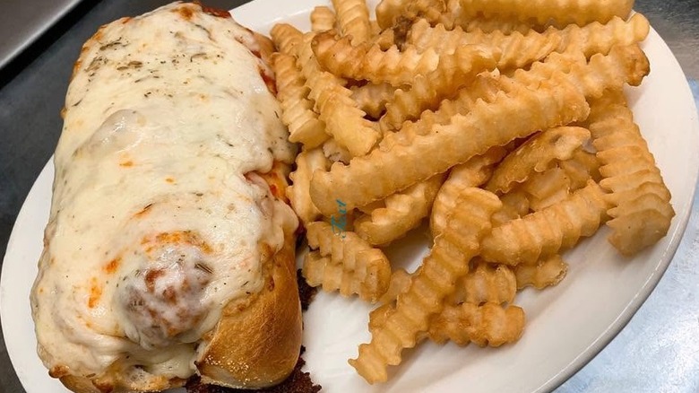 Plate holding a meatball sub sandwich doused with cheese and a side of crinkle-cut fries