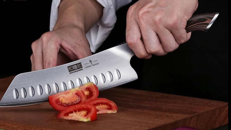 A person cutting a tomato with a Hoshanho santoku knife