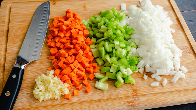 A santoku knife with chopped veggies on a wooden cutting board