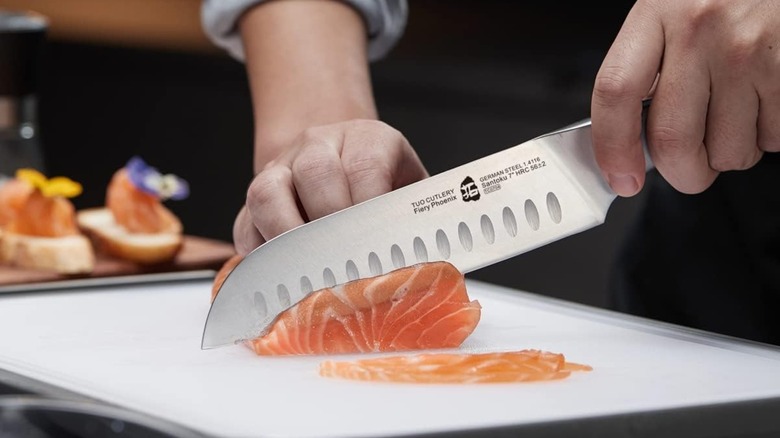 A person cutting salmon on a white counter with a Tuo Santoku knife