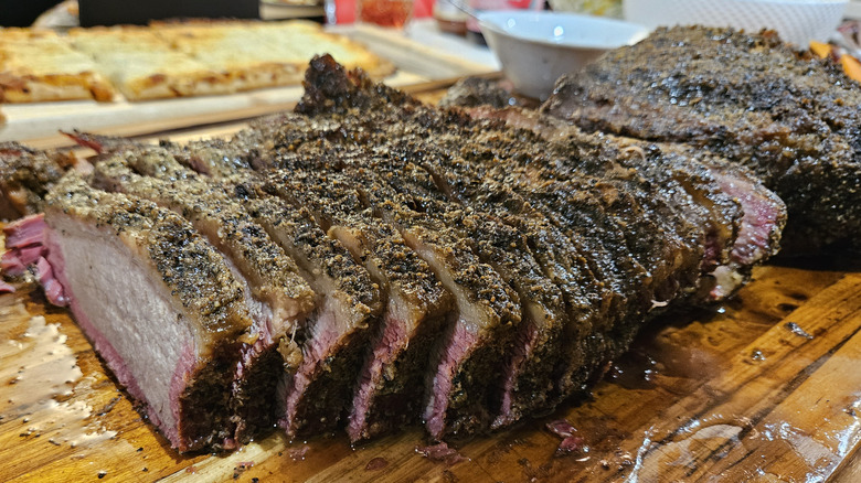 Sliced cooked steak covered in seasoning on cutting board.