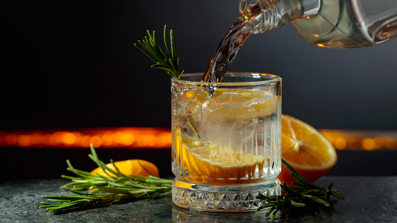 A liquor being poured into a garnished gin cocktail.