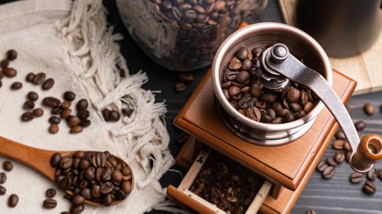 Whole coffee beans in manual grinder on wooden table