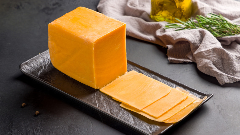 Slices of cheddar cheese on a cutting board next to a knife