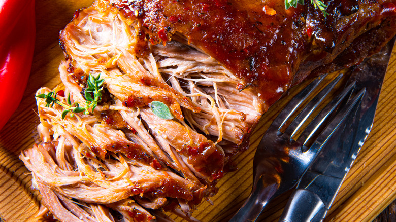 Pulled pork on wooden board beside silverware
